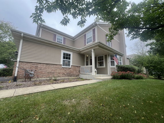 Front view of a two-story house with a porch and an American flag.