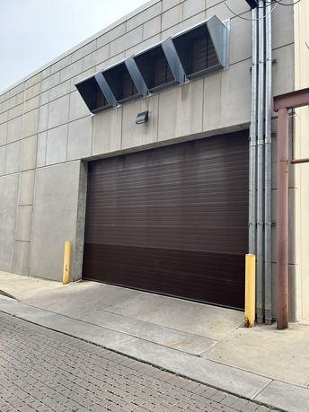 Front view of an industrial building with a large brown garage door and metal ventilation units.