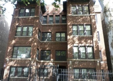 Front view of a multi-story brick building with several windows and an entrance gate.