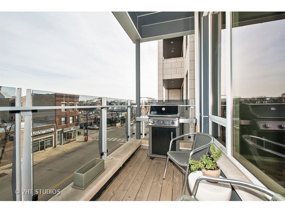 View from a balcony with outdoor furniture and a grill, overlooking a street.