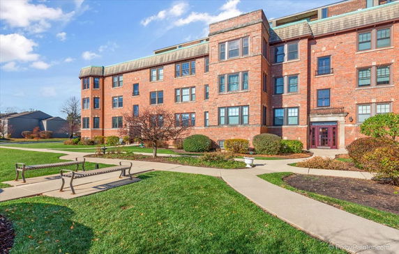 Front view of a multi-story brick apartment building with a landscaped pathway and benches.