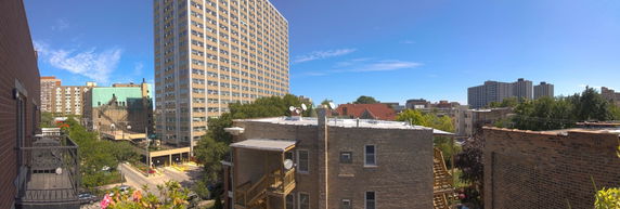 A wide-angle view from a building showing nearby apartment buildings and surrounding areas on a sunny day.