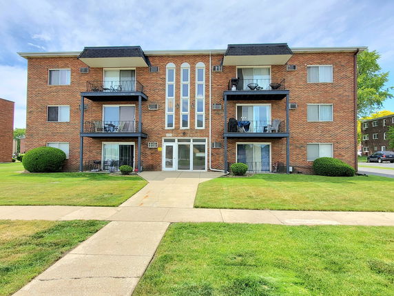 Front view of a three-story brick apartment building with balconies.