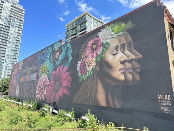 Side view of a tall building with a large mural featuring floral designs and faces.