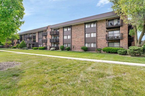 Front view of a three-story brick apartment building with balconies.