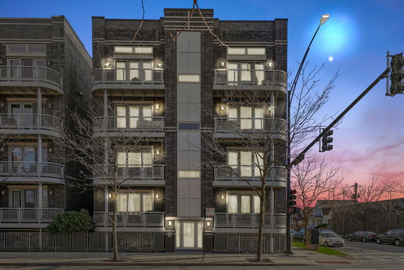 Front view of a multi-story building with balconies, seen at dusk with streetlights.