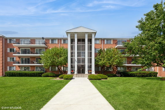 Front view of a multi-story apartment building with balconies and a central entrance.