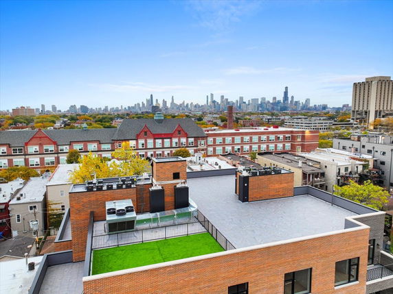 City skyline viewed from a rooftop with green artificial turf and brick structures.