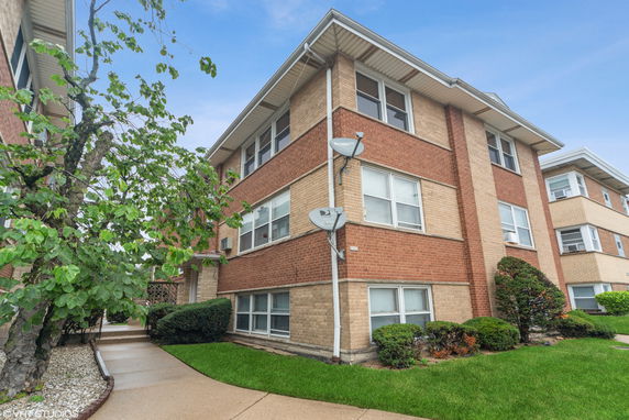Front view of a multi-story brick apartment building with rectangular windows and satellite dishes.