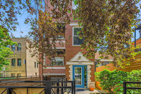 Front view of a multi-story brick building with a blue door and metal railing.