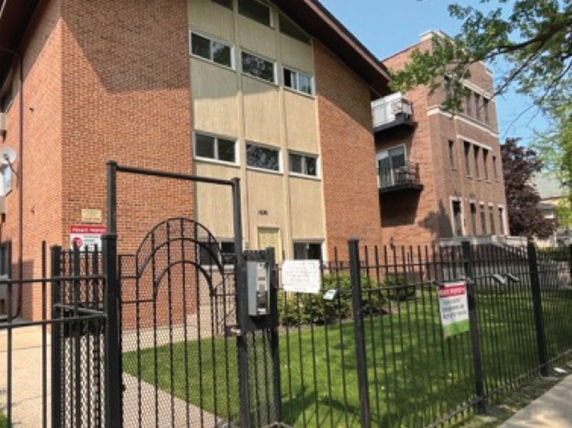 Front view of a multi-story brick building with a fenced entrance.