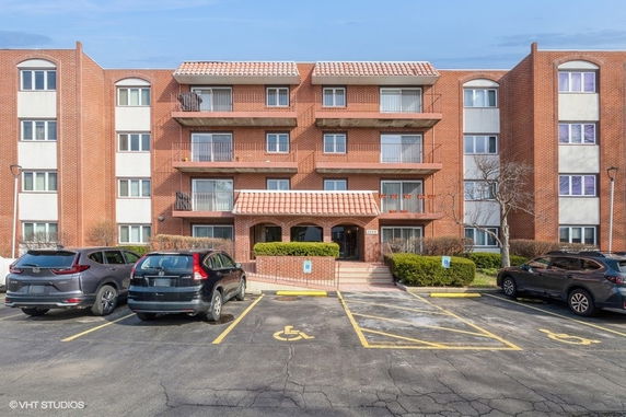 Front view of a multi-story brick residential building with balconies and a central entrance.