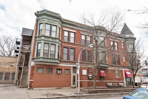Front view of a historic multi-story brick building with architectural details and a corner turret.