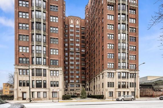 Front view of a tall brick apartment building with multiple windows and detailed stonework at the base.