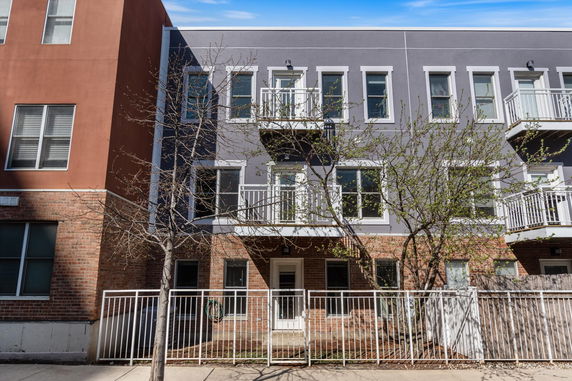 Front view of a multi-story residential building with balconies and a fenced entrance.