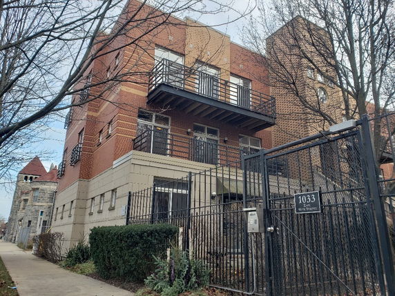Front view of a multi-story brick building with metal balconies and a gated entrance.
