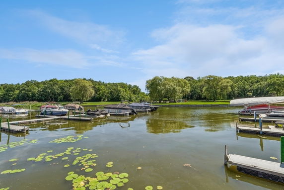 View of a marina with boats docked on a calm body of water surrounded by trees.