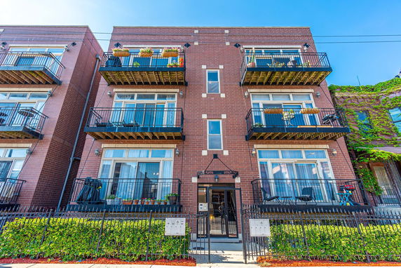 Front view of a three-story brick apartment building with balconies and a gated entrance.