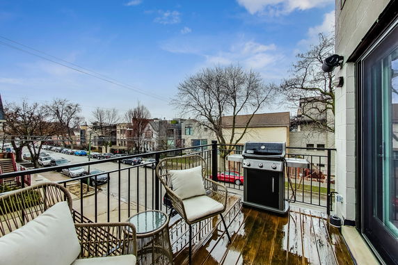 Balcony view overlooking residential street with outdoor seating and grill.