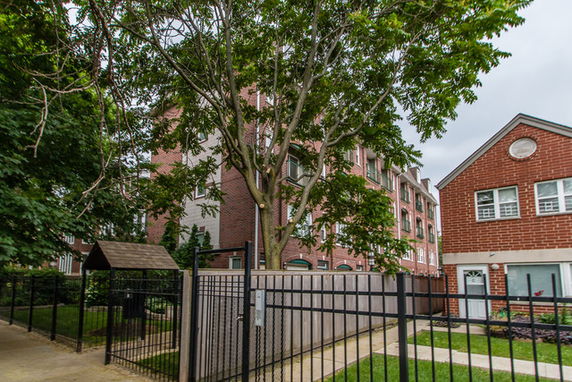 Front view of a multistory brick building with trees and a fence.