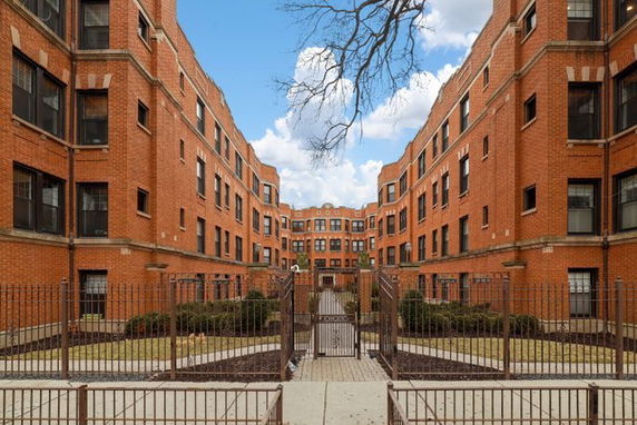 Front view of a multi-story brick apartment building with a gated entry.
