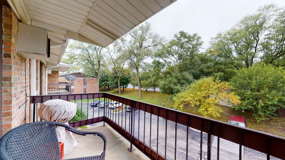 Balcony view overlooking a parking area and trees.