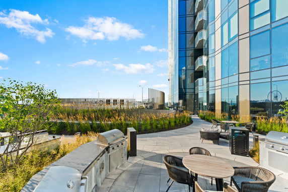 Rooftop area with outdoor seating and barbecue grills adjacent to a modern glass building.