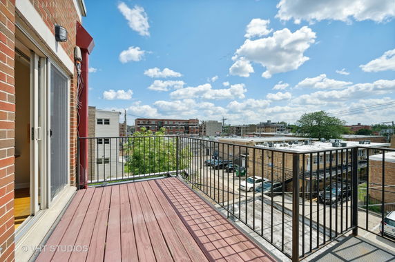 View from a balcony showing nearby buildings and a clear blue sky.