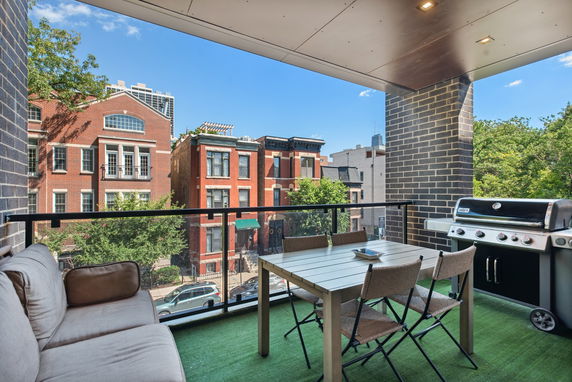 Balcony view overlooking residential brick buildings with outdoor seating and grill.