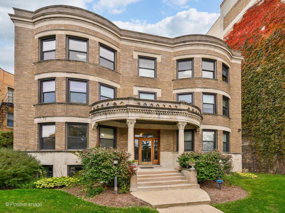 Front view of a brick three-story building with a covered entrance and large windows.