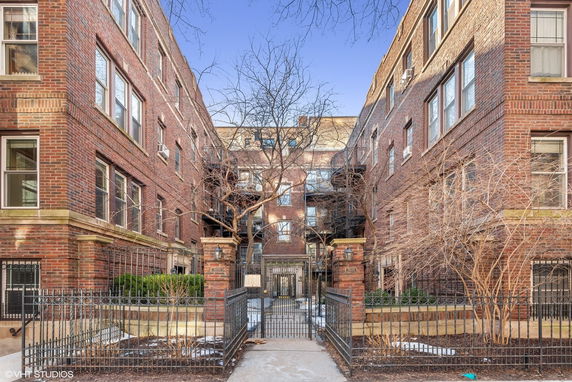 Front view of a multi-story brick apartment building with iron gates and bare trees at the entrance.