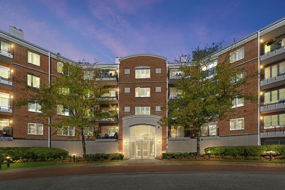 Front view of a multi-story brick apartment building with balconies and illuminated entrance.