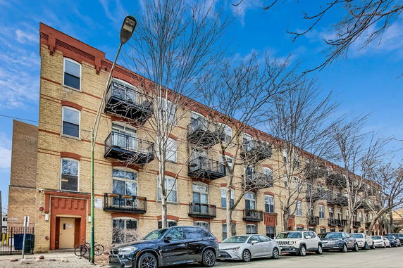 Front view of a multi-story brick building with balconies and parked cars.