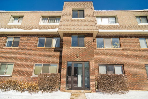 Front view of a brick multi-story apartment building with multiple windows and a central entrance.