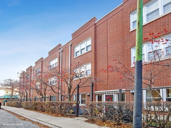 Front view of a multi-story brick building with large windows and a fence.