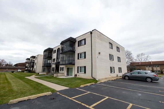 Front view of a three-story apartment building with balconies and parking area.