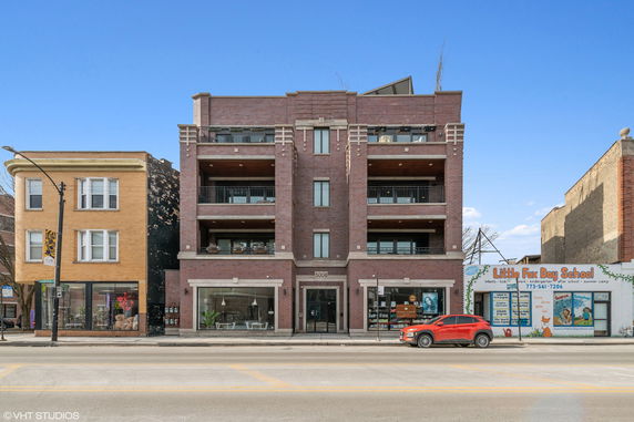 Front view of a multi-story brick building with balconies and shops on the ground floor.