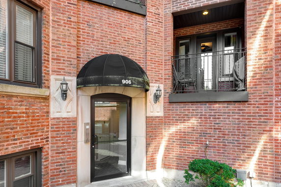 Front view of a brick building with an arched entrance and a small balcony above the door.
