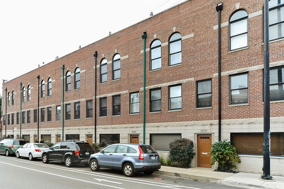 Front view of a three-story brick townhouse with arched windows and multiple entrances.