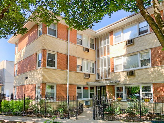 Front view of a three-story brick apartment building with a fenced entrance.
