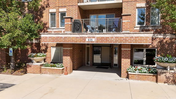 Front view of a brick building with balcony and flower beds.