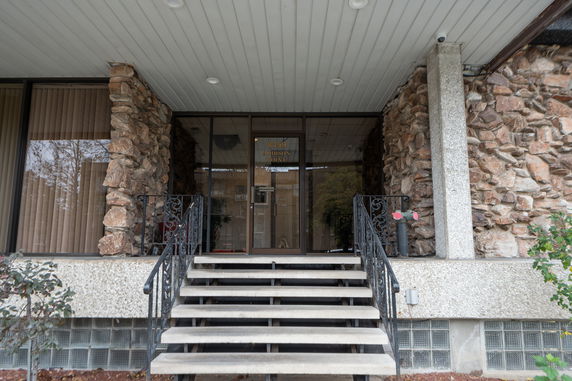 Front view of a building entrance with stone facade and stairs leading to glass doors.