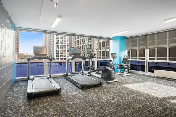 Interior view of a gym area with exercise equipment and large windows.