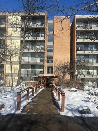 Front view of a multi-story apartment building with balconies and an entrance walkway.