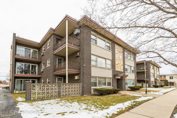 Front view of a three-story apartment building with balconies and brick exterior.