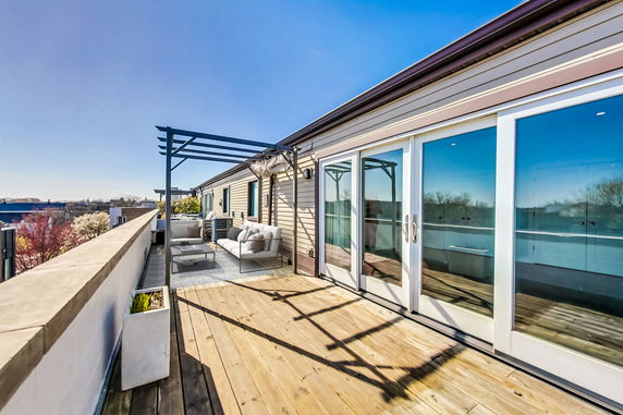 Rooftop terrace with seating area and pergola, featuring sliding glass doors.