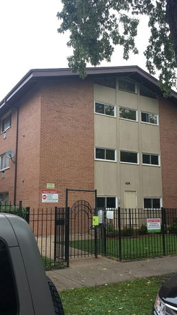 Front view of a multi-story brick apartment building with a gated entrance.