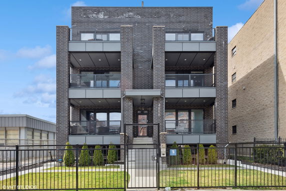 Front view of a multi-story brick building with balconies and a gated entrance.