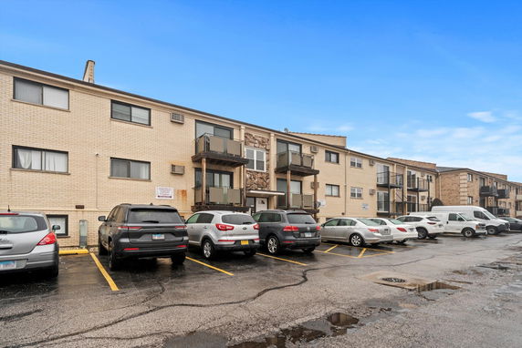 Front view of a multi-story apartment building with balconies and outdoor parking.