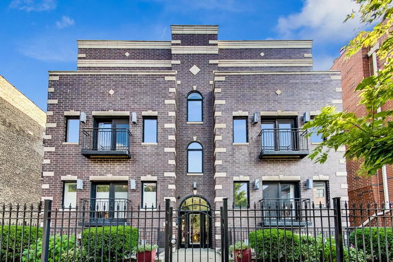 Front view of a brick multi-story building with decorative balconies and an arched entrance.
